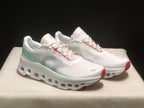 Front three-quarter view of the pair highlighting the white uppers, pale green side panels, gray branding, and red toe accents.