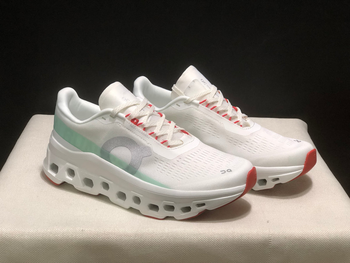 Front three-quarter view of the pair highlighting the white uppers, pale green side panels, gray branding, and red toe accents.