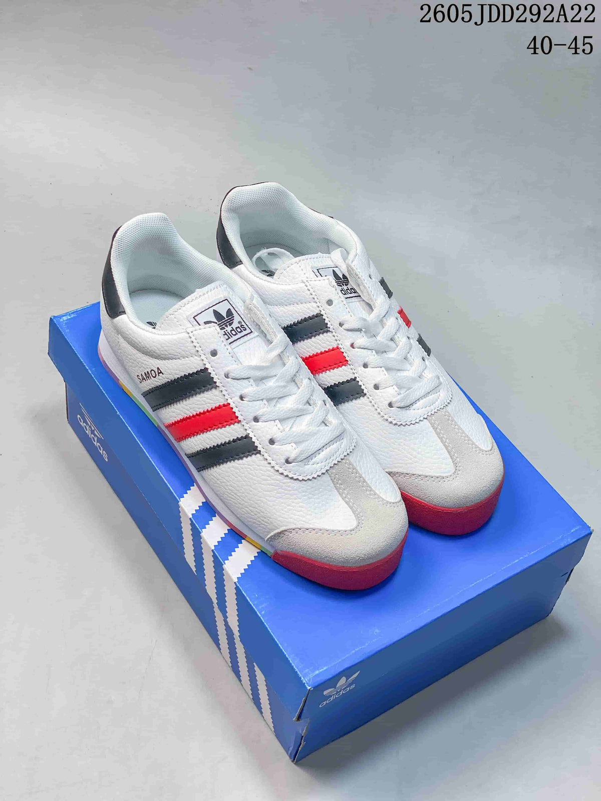 Pair of white adidas Originals Samoa sneakers with black and red stripes, shown on a blue adidas shoebox.