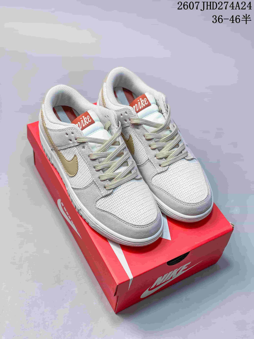 Pair of white and light gold Nike SB Dunk Low Pro sneakers displayed on a red shoebox.