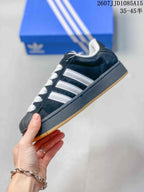 Side view showing the black upper, white three-stripe detailing, raised midsole, and gum outsole.