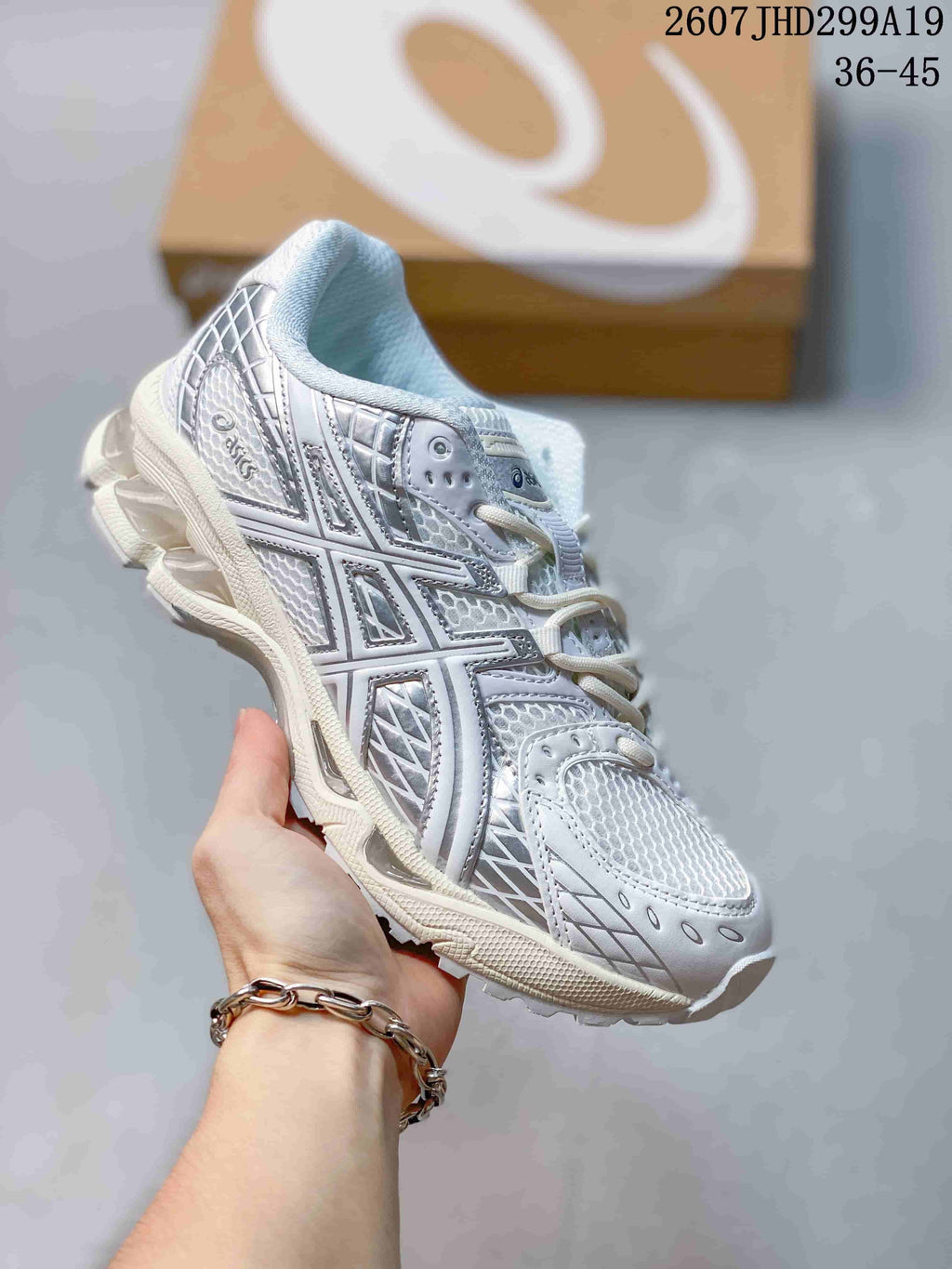 White and silver ASICS Gel-Nimbus 10.1 sneaker with layered panels and a thick cream-toned sole; image text shows style code 2607JHD299A19 and size range 36-45.