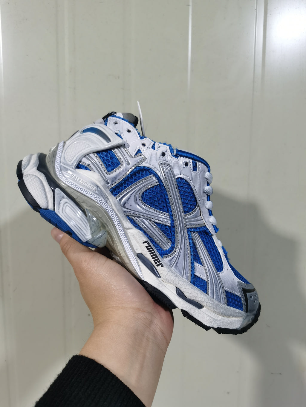 Angled close-up of the white and blue Runner sneaker showing the layered upper, heel structure, and contrasting outsole.