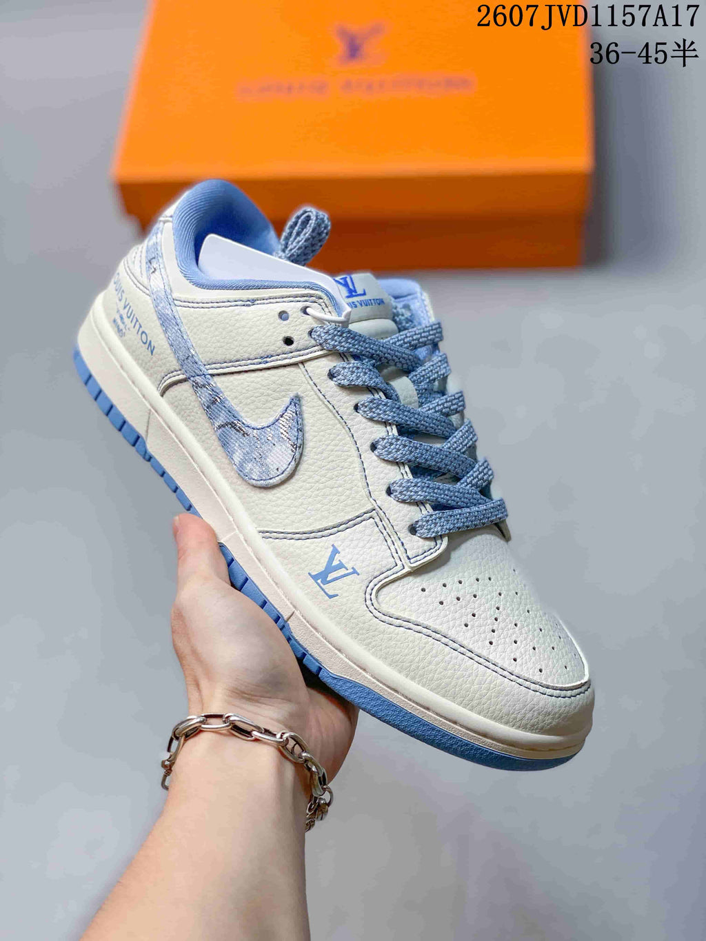 White low-top sneaker with pale blue denim-inspired swoosh-style overlays, blue laces, and Louis Vuitton-style branding.