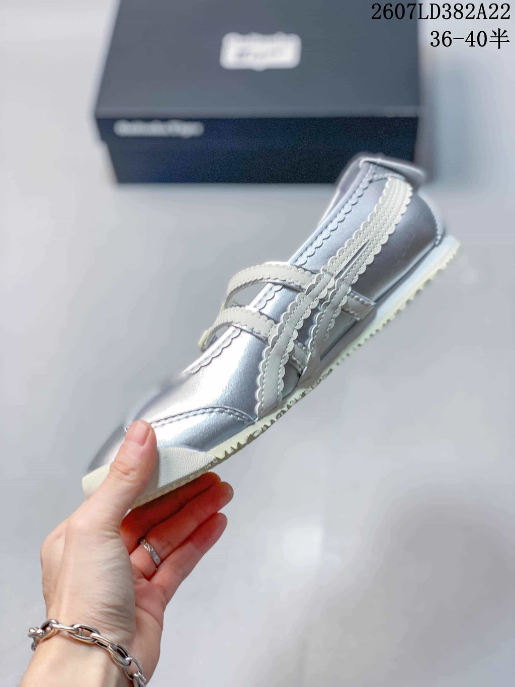 Side view of the silver low-top sneaker showing the layered side detailing, buckle straps, and light outsole.