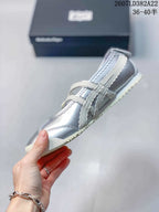 Side view of the silver low-top sneaker showing the layered side detailing, buckle straps, and light outsole.