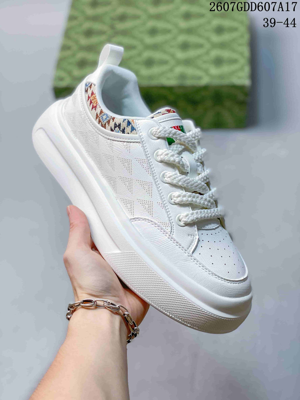 Close side view of a white Gucci sneaker with patterned collar trim, padded lining, white laces and a layered rubber sole.