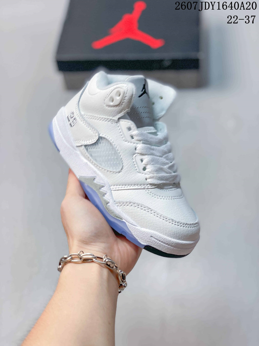 Side three-quarter view of the white kids' sneaker showing the lace area, layered upper, and light-blue outsole.