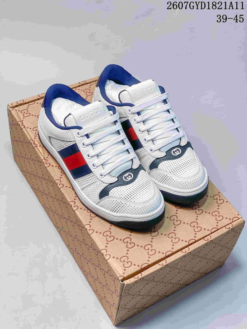 Pair of white Gucci-branded low-top sneakers with navy and red side stripes displayed on a patterned shoe box.