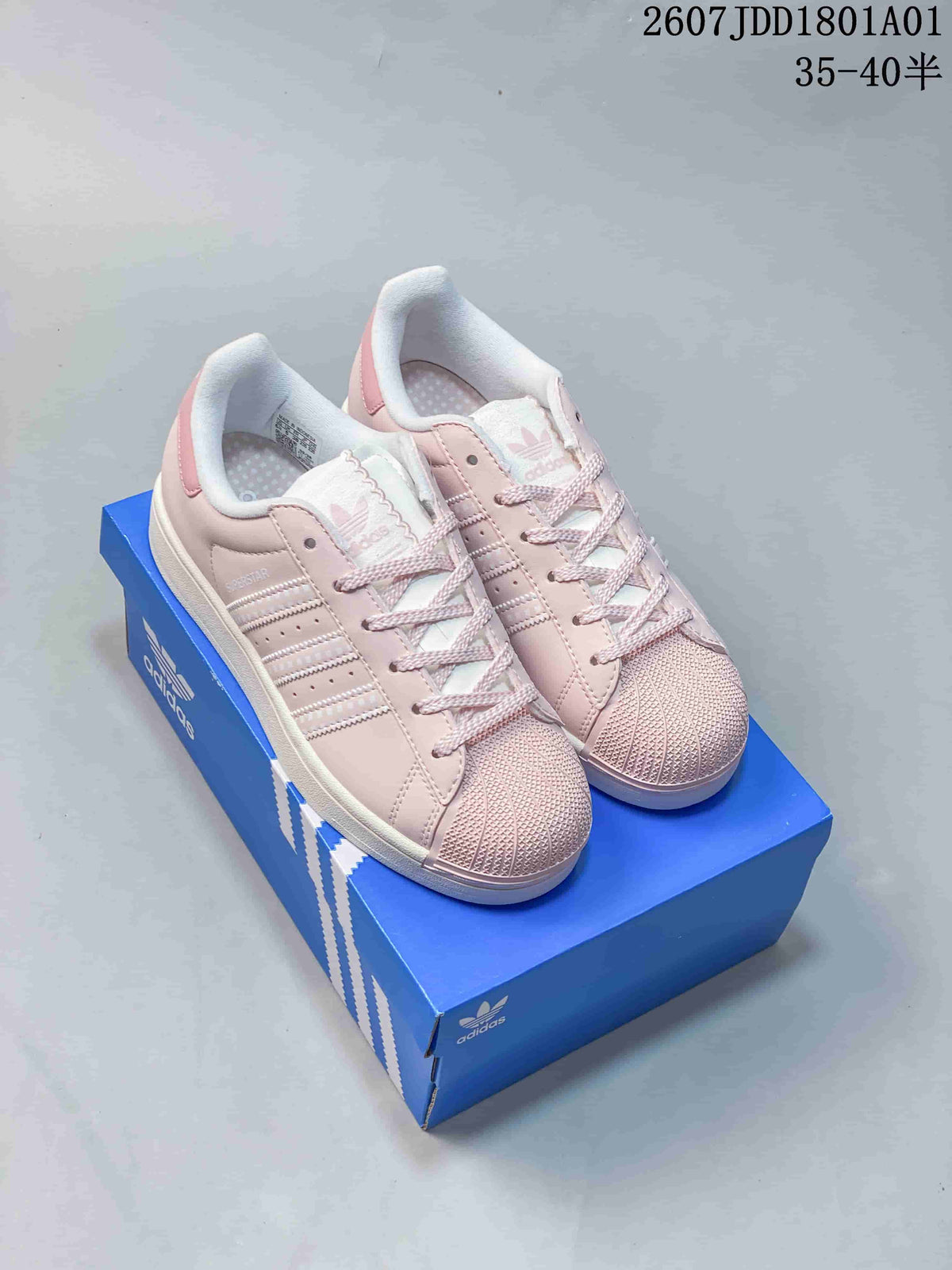 Pair of pastel pink Adidas Superstar sneakers on a blue shoebox