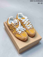 Pair of mustard and tan New Balance sneakers with white laces displayed on a branded shoebox; Miu Miu tongue labels are visible.