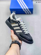 Angled side view of a black and white sneaker with white stripes, gold Spezial branding and a textured black sole.