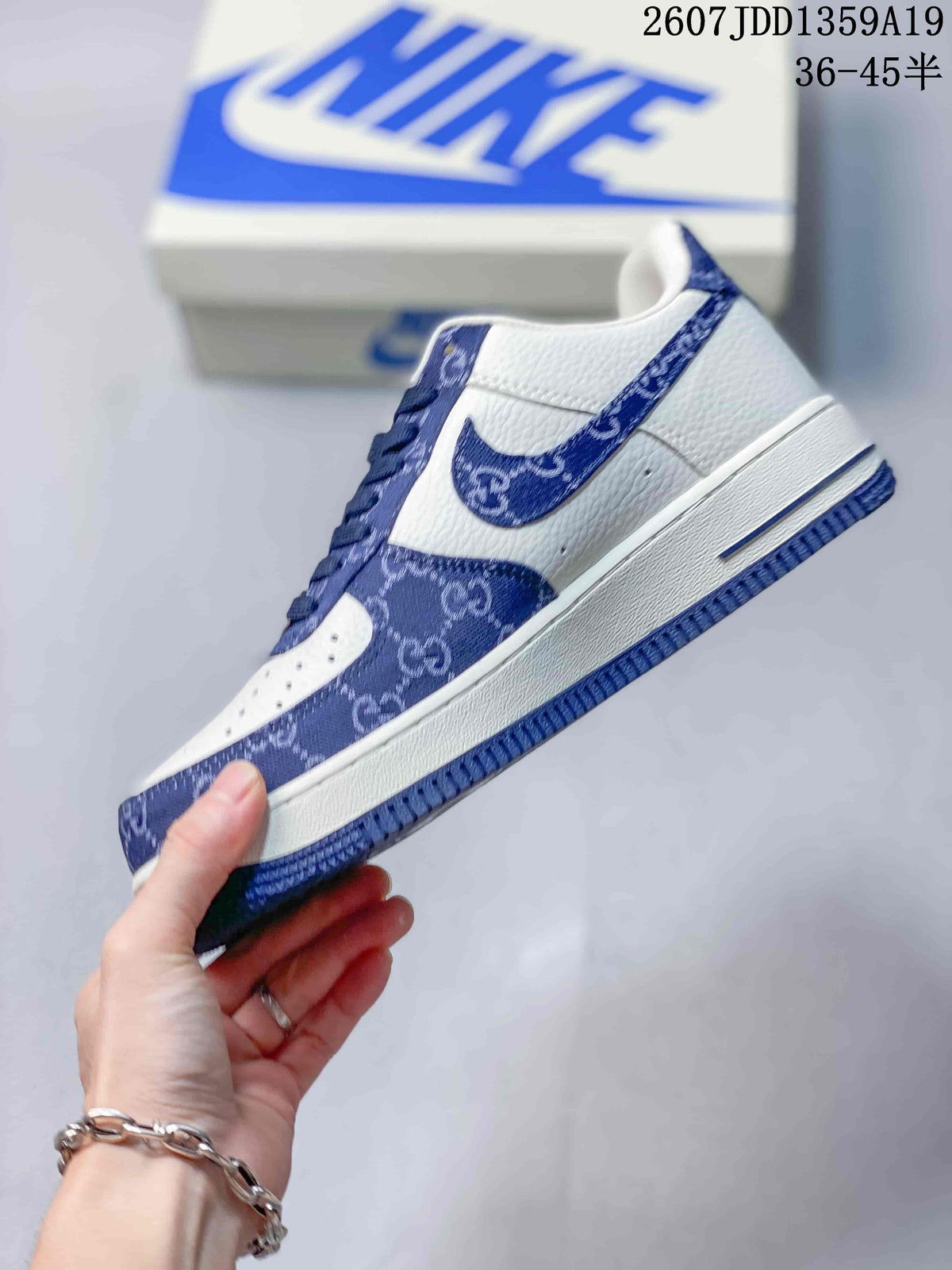 Side view of a white low-top sneaker with blue patterned overlays, a blue Swoosh-style detail, and a white midsole.