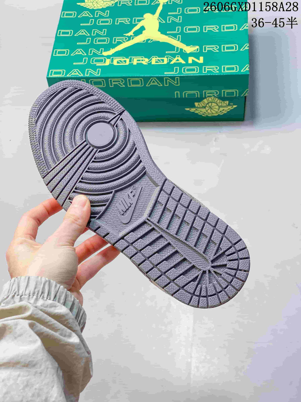 Close-up of the textured outsole of the grey Air Jordan 1 sneaker beside its box