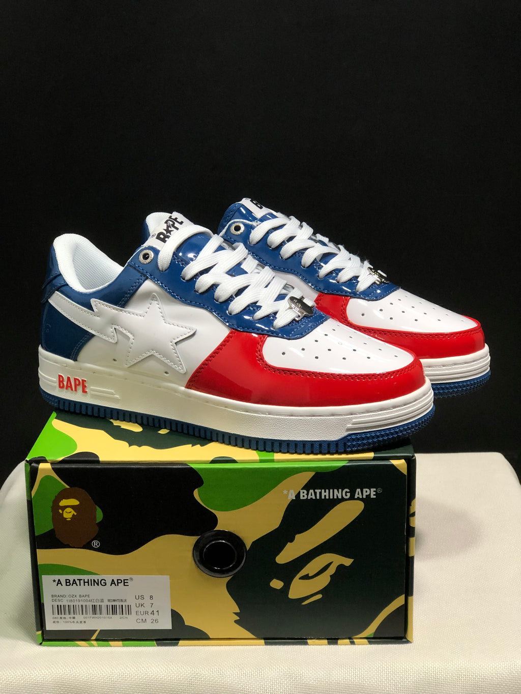 Pair of white, blue, and red Bape Sta sneakers displayed on a branded camouflage shoe box.