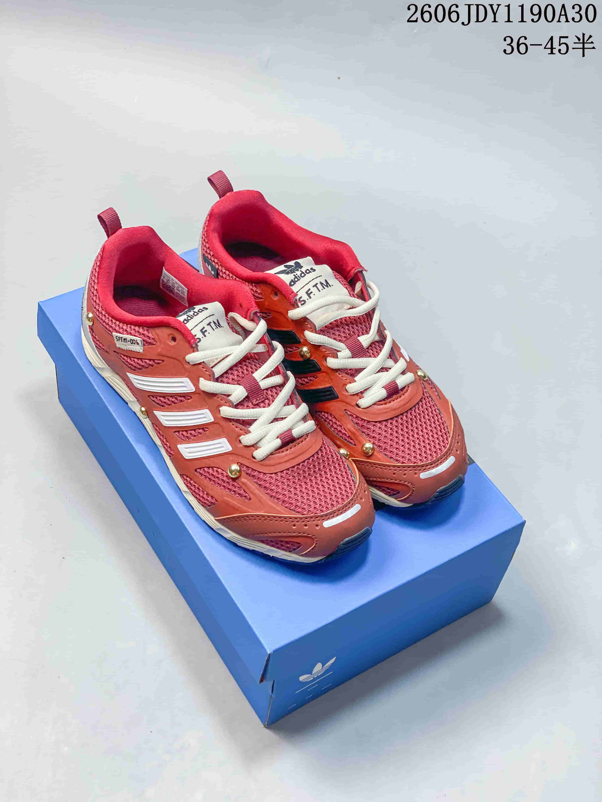 Pair of rose and coral adidas Adizero PR SFTM-006 sneakers on a blue box.