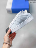 Side profile showing the white upper, layered three-stripe panels, black shell toe, and white platform-style sole.