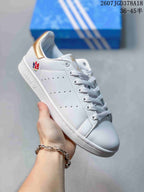 Angled side view showing the white sneaker, perforated side stripes, gold heel tab and rubber outsole.