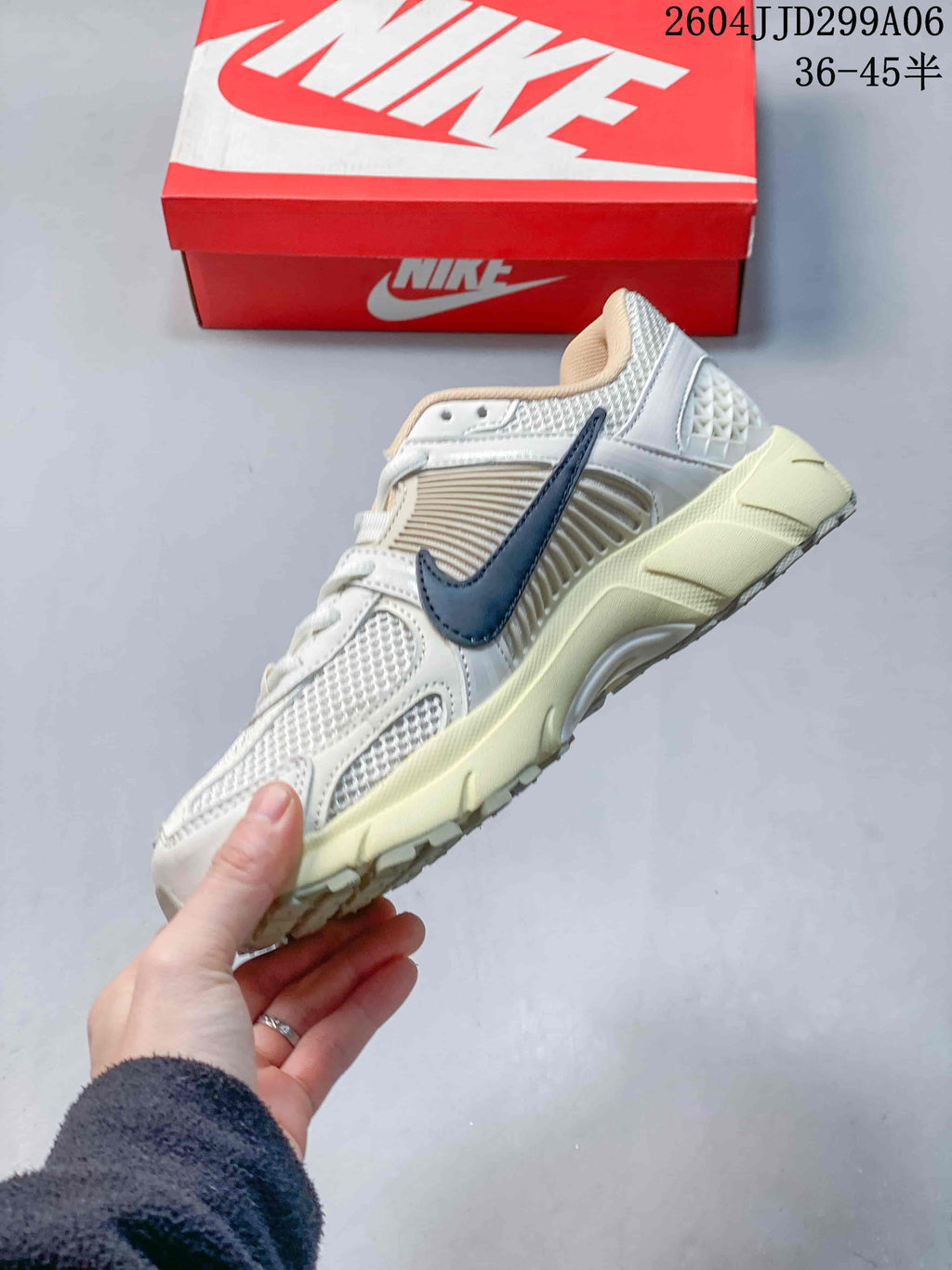Side profile of a Nike Zoom Vomero 5 sneaker with layered panels, navy Swoosh, and cream midsole.