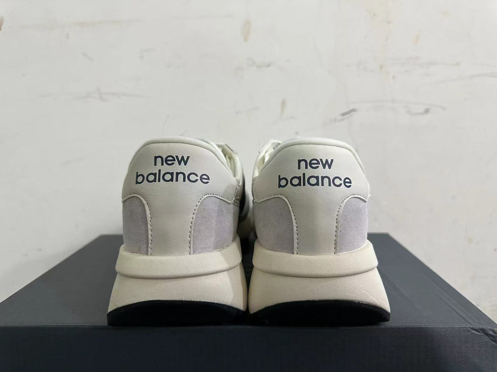 Rear view of gray and off-white New Balance U370 sneakers with navy heel branding.