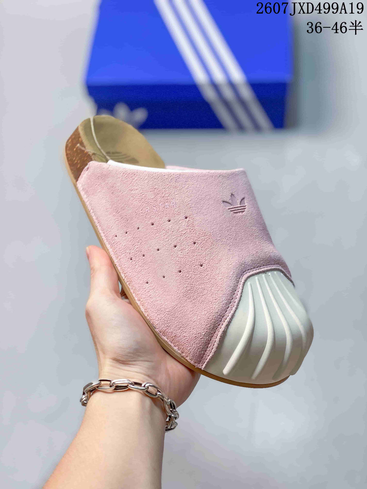 Close-up side view of a pink closed-toe mule slide showing perforations, Trefoil branding and a ribbed white toe detail.