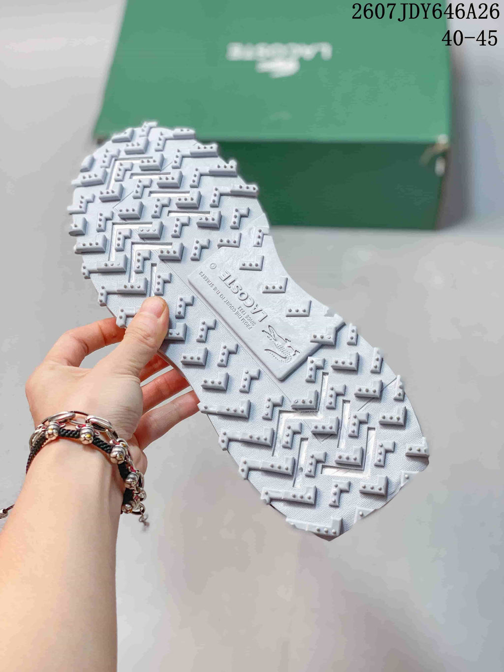 Close view of the textured white lugged outsole of the Lacoste sneaker, with the green shoe box in the background.