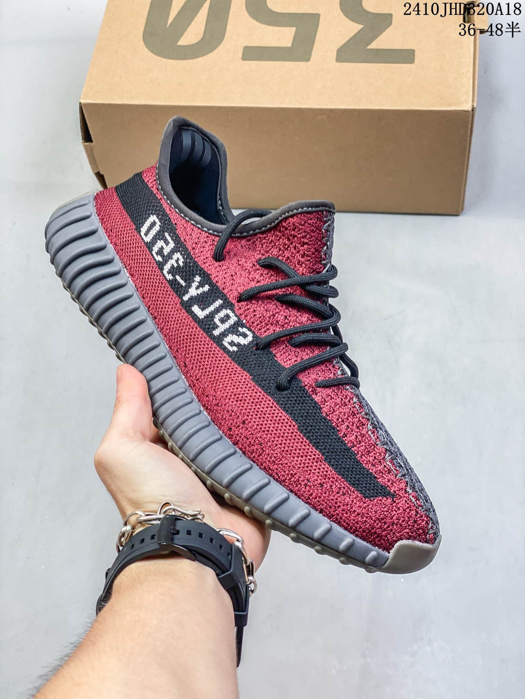 Side profile of the red Adidas Yeezy Boost 350 V2 sneaker showing the black side stripe with lettering and ribbed gray outsole.