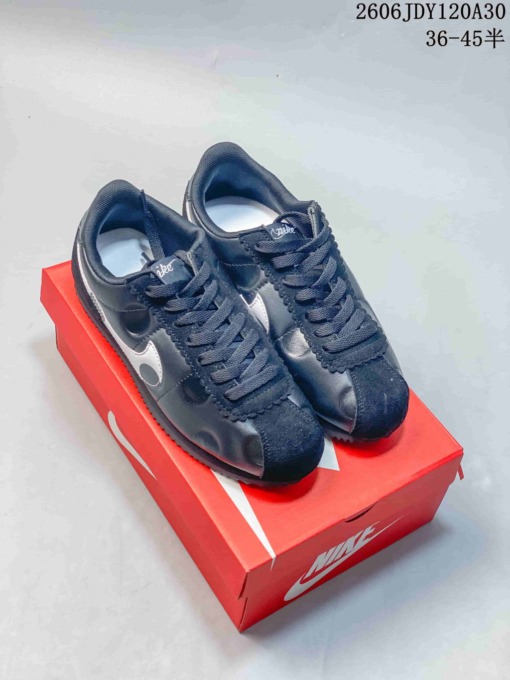 Pair of dark Nike Classic Cortez sneakers with silver side detailing on a red shoe box