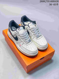 Pair of white low-top Nike Air Force 1 style sneakers with dark accents and patterned laces on an orange box