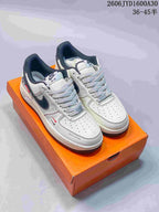 Pair of white low-top Nike Air Force 1 style sneakers with dark accents and patterned laces on an orange box