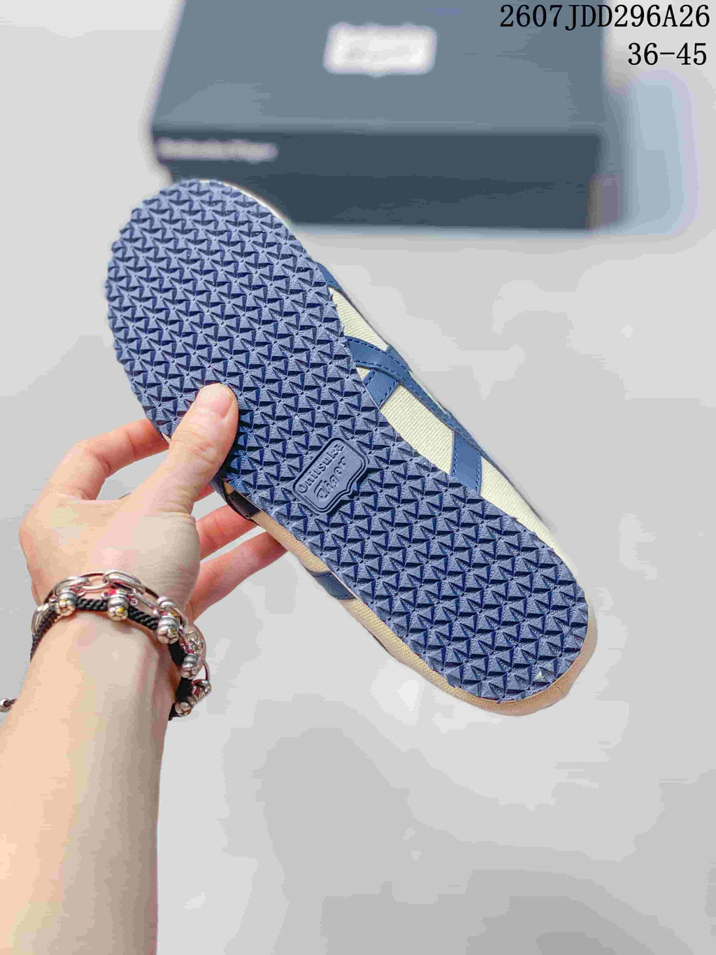 Close view of the patterned navy rubber outsole on a cream and navy Onitsuka Tiger sneaker; image text shows size range 36-45.