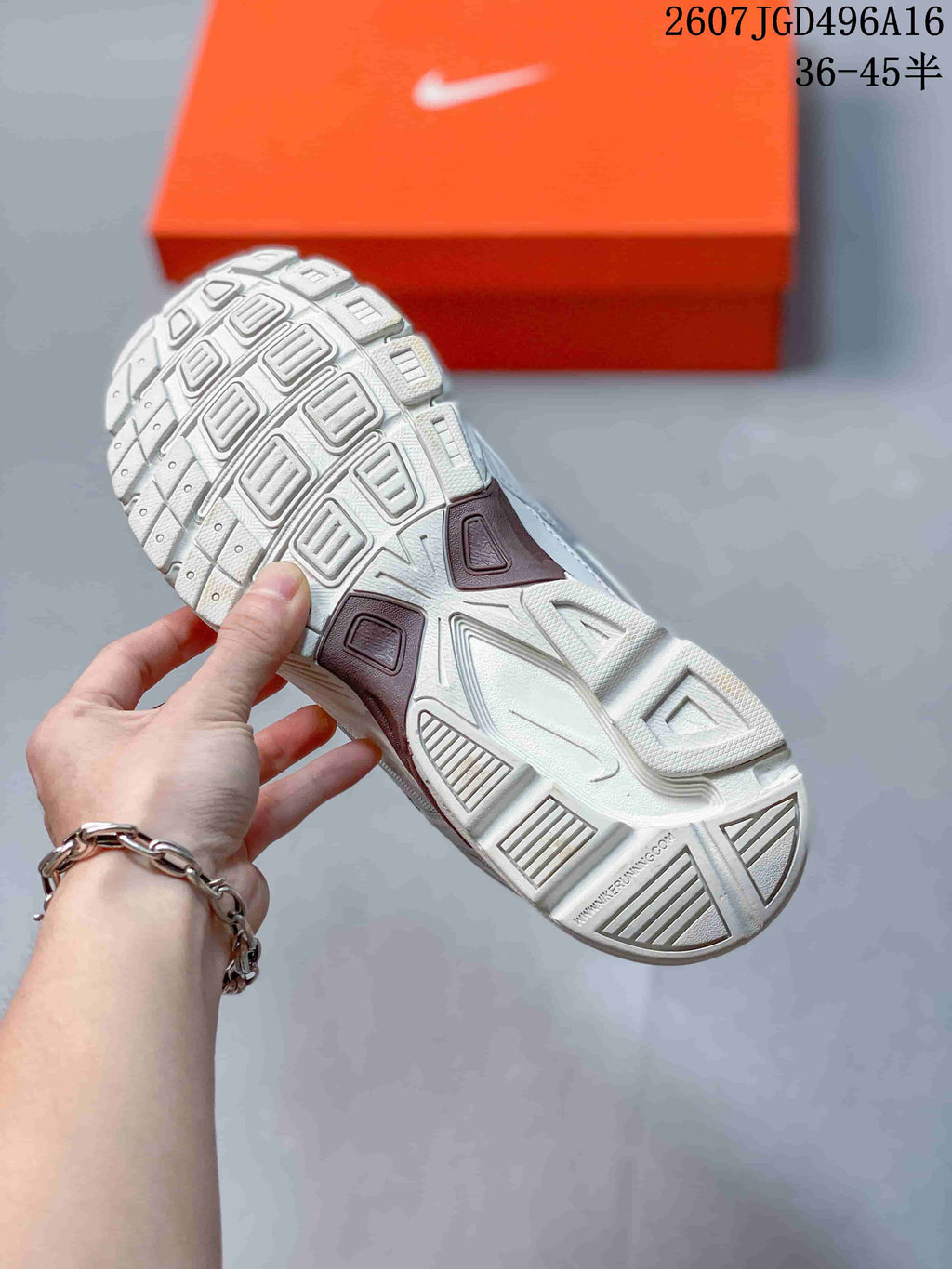 Underside view of a Nike Initiator sneaker showing the segmented textured outsole and orange shoebox in the background.