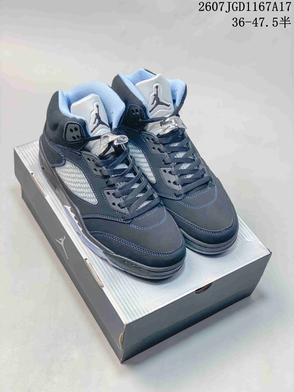 Pair of black Jordan Air Jordan 5 high-top sneakers displayed on a shoebox, showing blue-gray stitching, padded collars and translucent outsoles.