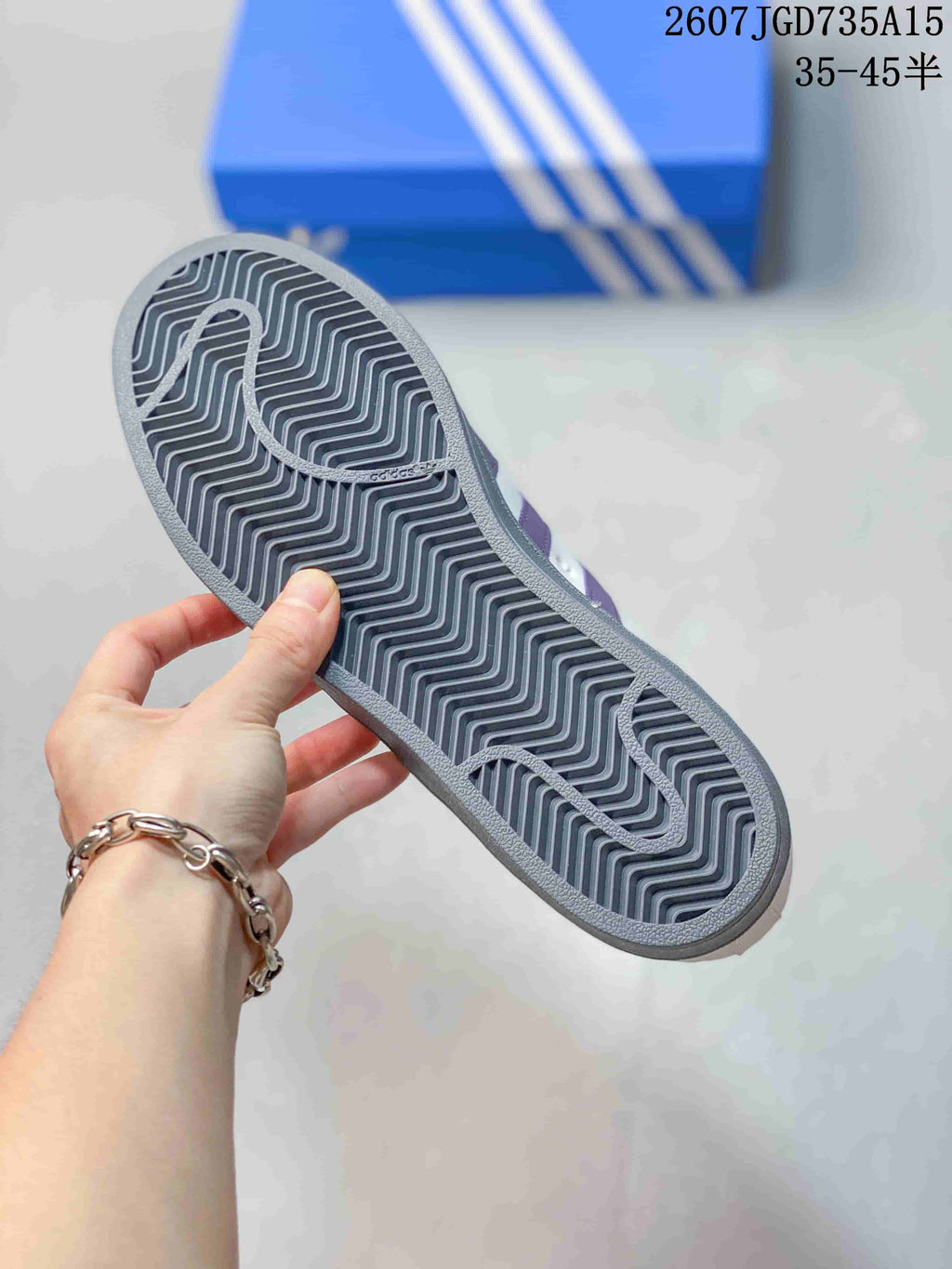 Close-up of the gray patterned outsole with a zigzag tread design, held above a blue Adidas shoebox.