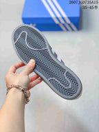 Close-up of the gray patterned outsole with a zigzag tread design, held above a blue Adidas shoebox.