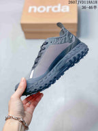 Side profile of the gray Norda sneaker showing the patterned upper, lace system, layered midsole, and lugged outsole.