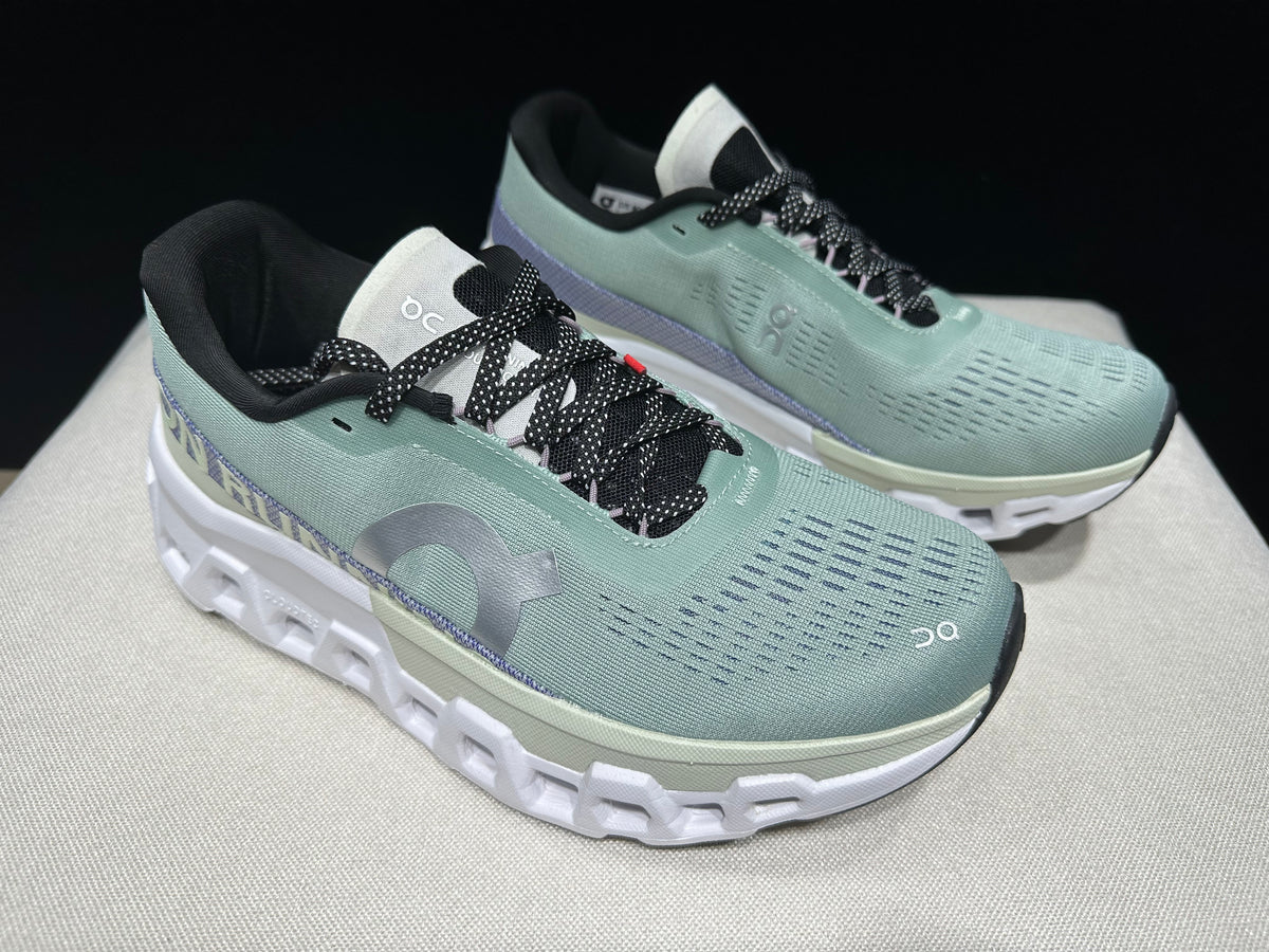 Angled top view of the pair with black-and-white laces and pale green uppers.