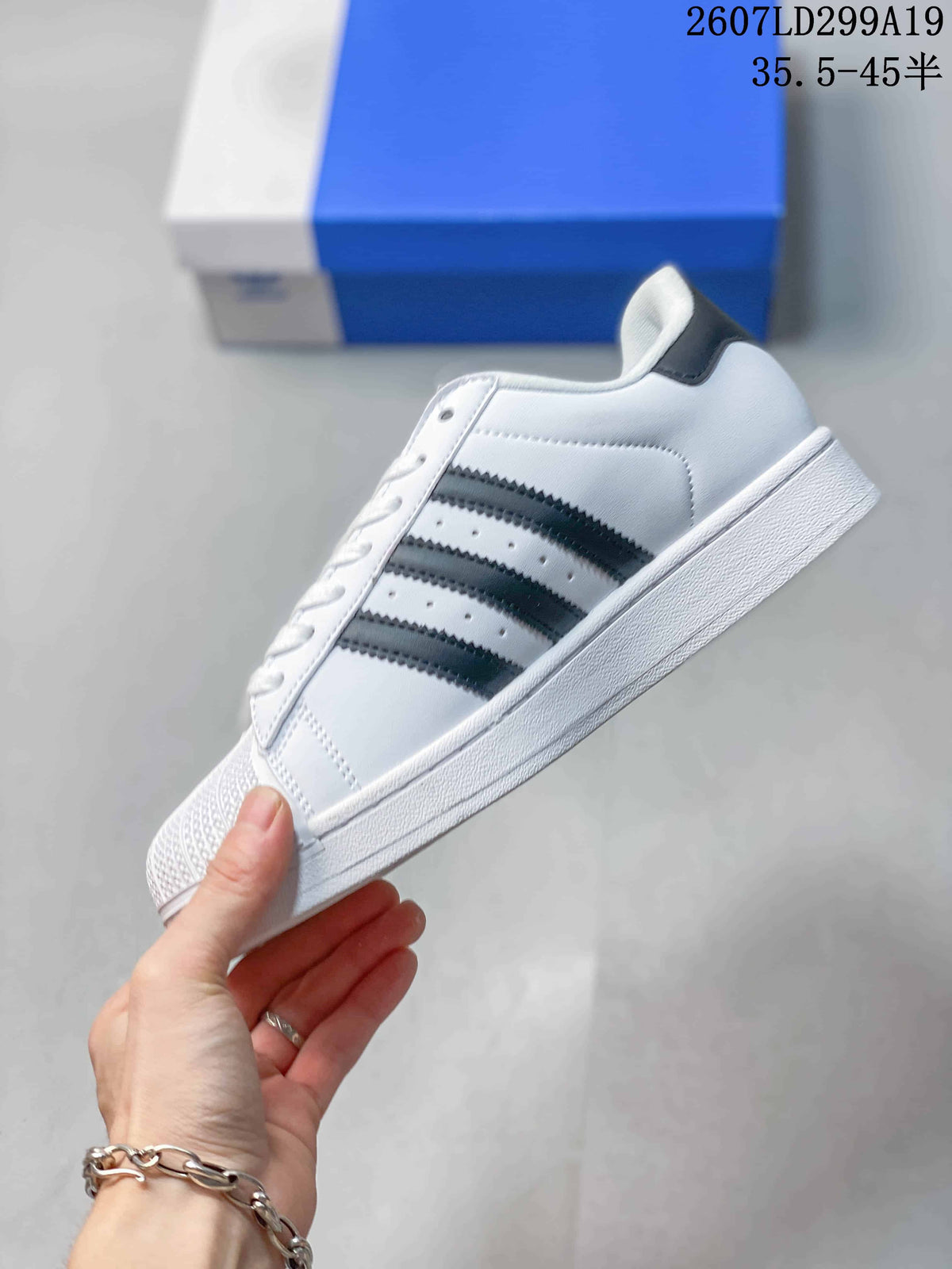 Side view of a white adidas Superstar sneaker with black three-stripe detailing, perforated side panels and a white sole.