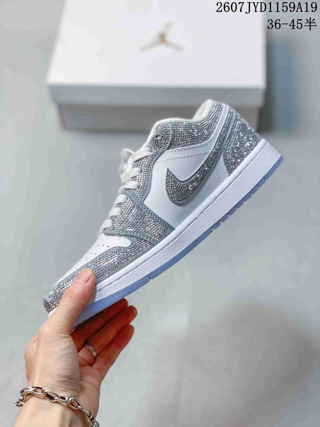 Side profile of a white low-top sneaker with silver decorative overlays, swoosh detail, white midsole, and translucent outsole.