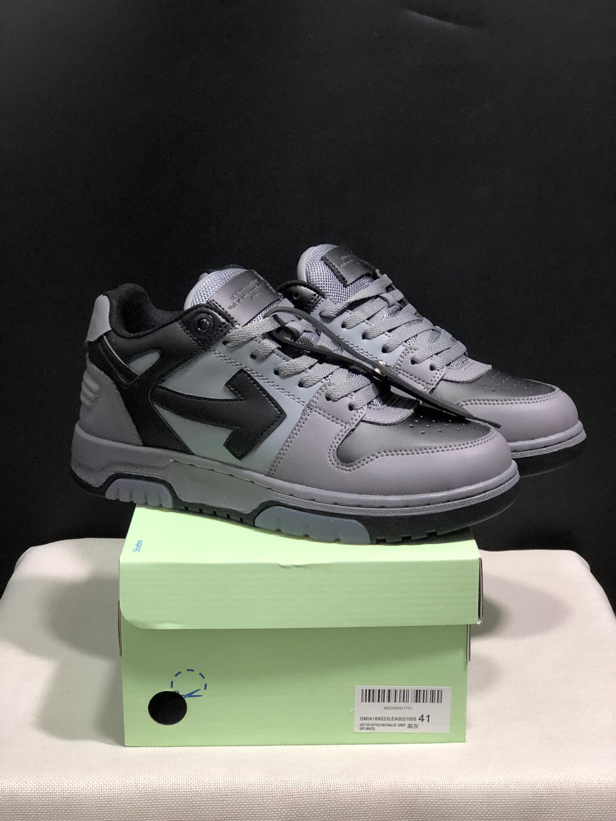 Pair of grey and black OFF-WHITE Out Of Office sneakers displayed on a pale green shoe box.
