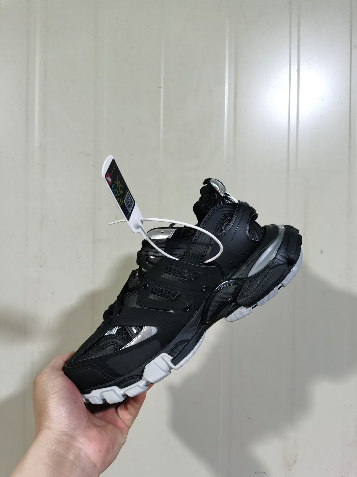 Angled view of the black and silver Balenciaga sneaker showing layered panels, lace closure, silver accents, and segmented white outsole details.