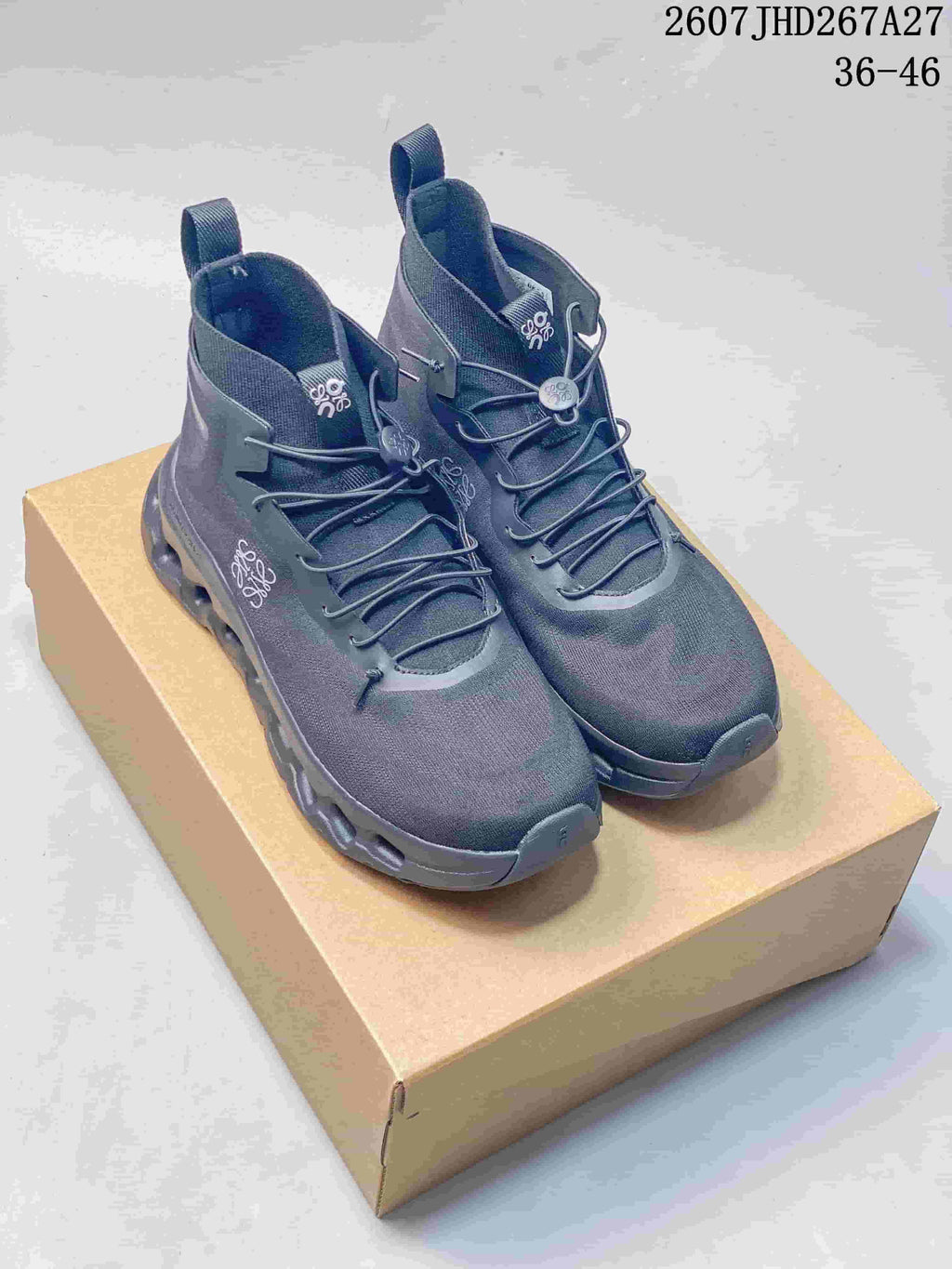 Pair of dark gray LOEWE x On Cloudtilt high-top sneakers displayed on a tan shoebox, with the 36-46 size range and source code visible at the top.