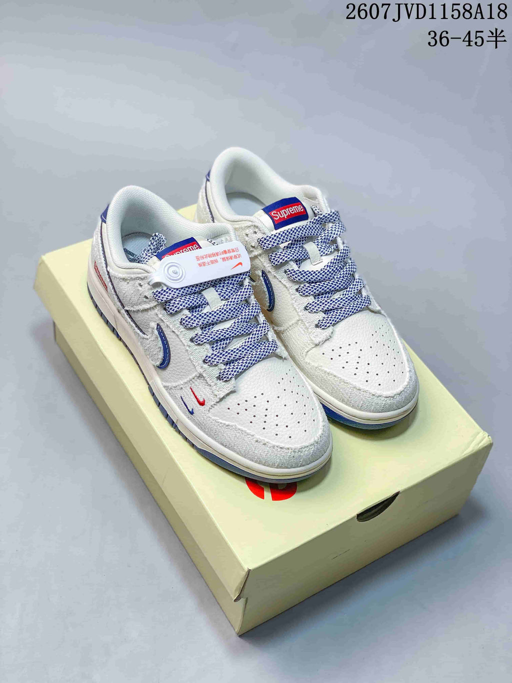 Pair of white and gray sneakers with blue accents, patterned laces, and red and blue tongue branding on a light-colored box.