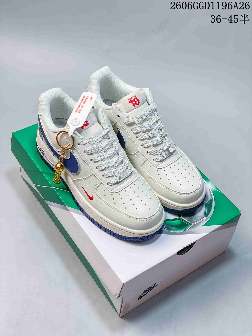 White low-top sneakers with blue side accents, red details, and a hanging charm, pictured on a green-and-white box.