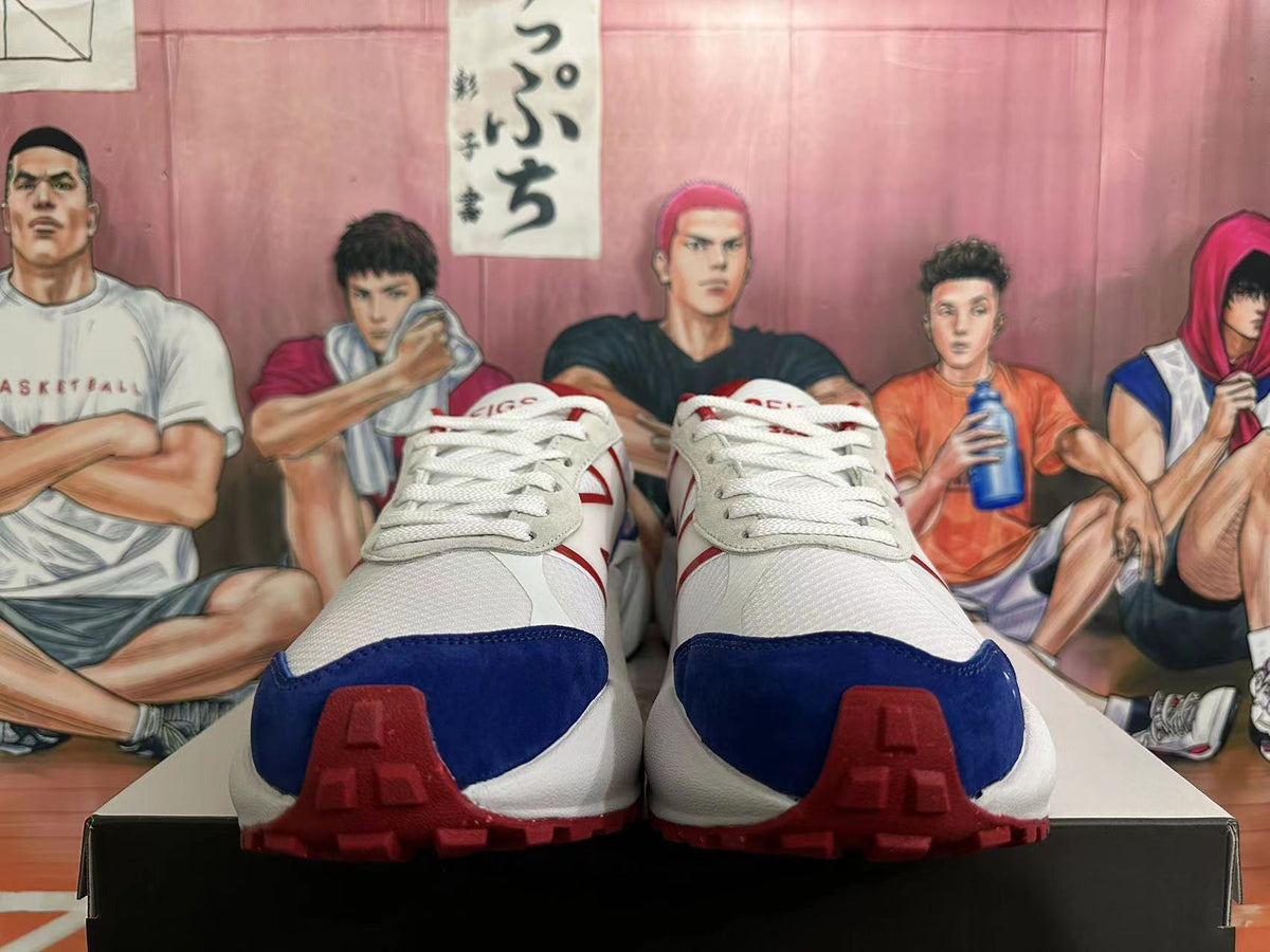 Front view of white New Balance sneakers with navy toe overlays, red details, and white laces.