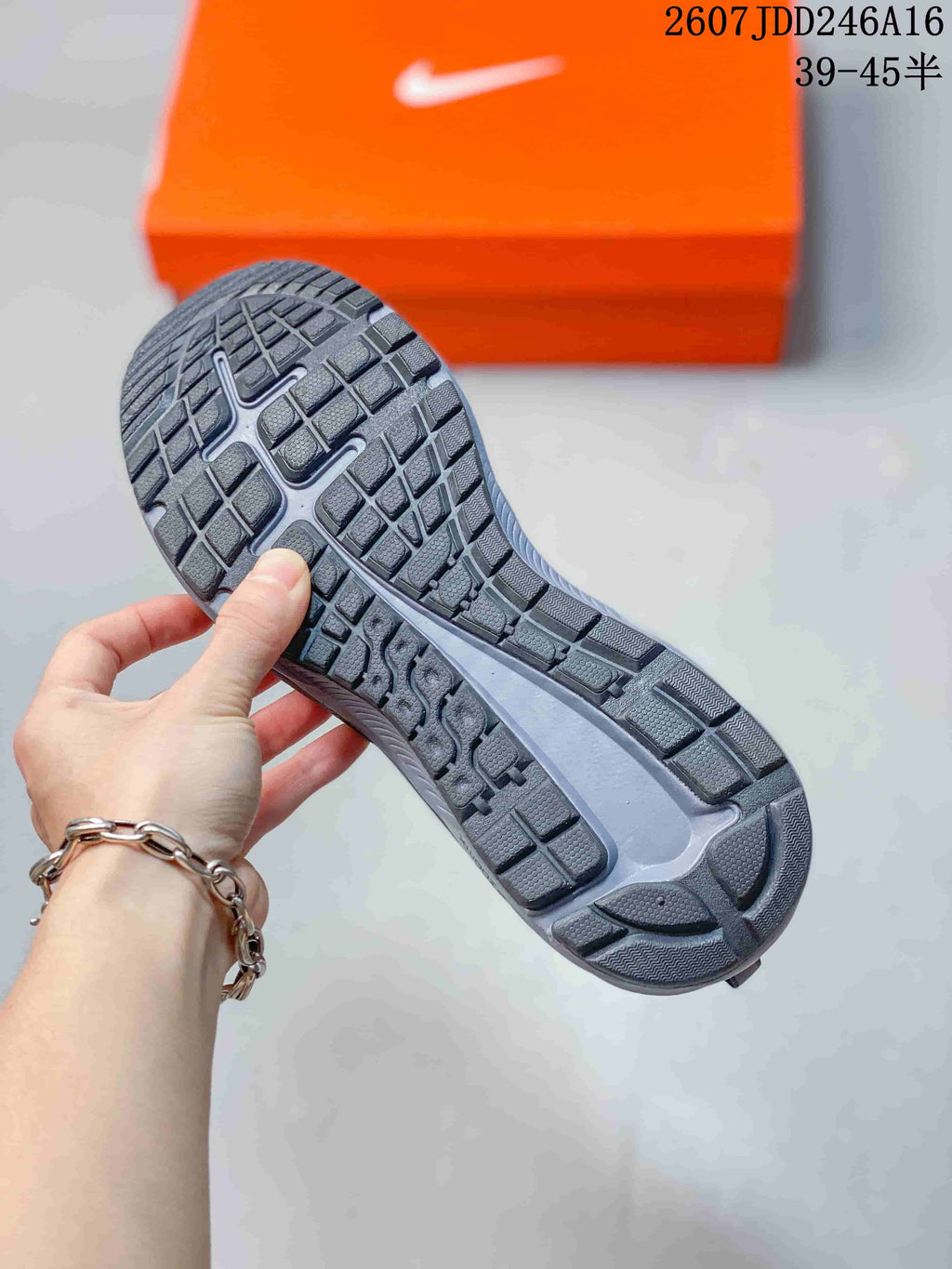 Close-up of the textured outsole showing segmented tread blocks and a central Nike-shaped detail, with an orange shoebox in the background.