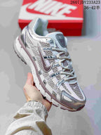 Side view of a white and silver Nike P-6000 sneaker highlighting the mesh upper, layered overlays, padded collar, and textured outsole; the image shows style code 2607JDY233A23 and size range 36–42.