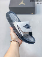 Angled side view of a white and navy Nike Air Jordan slide with adjustable strap, textured footbed, and layered outsole.