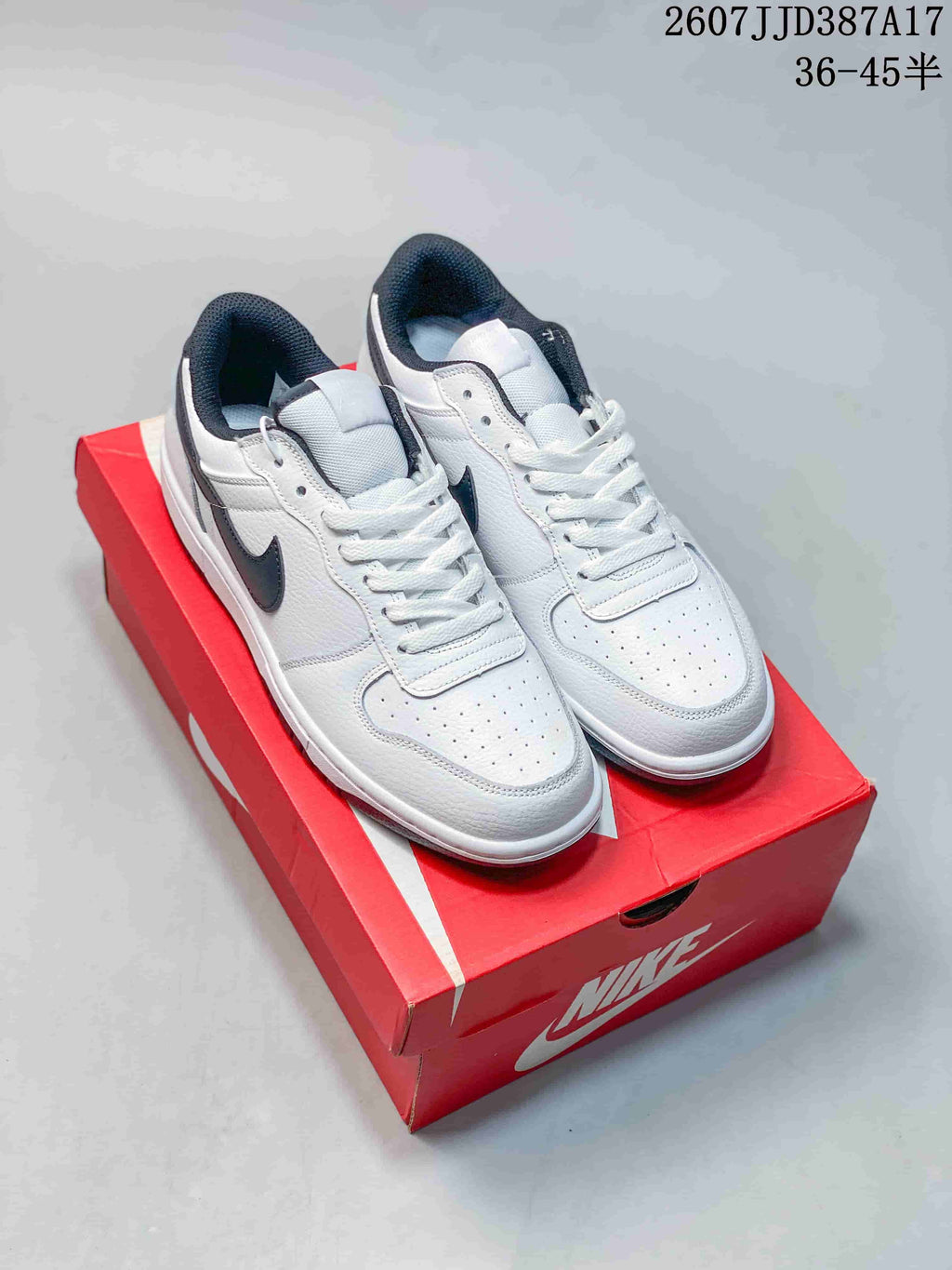 Pair of white and black Nike low-top sneakers displayed on a red Nike shoebox.