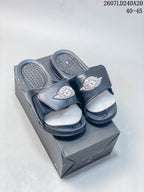 Pair of dark Jordan slides with adjustable straps displayed on a shoebox; image text shows style code 2607LD240A20 and size range 40–45.